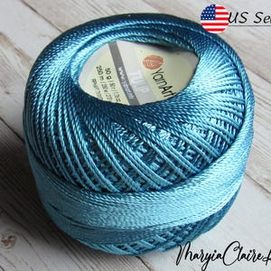 May include: A teal blue ball of yarn with a white label that reads "YarnArt TULIP" and "50g / 1.76 oz / 250 m / 273 yds".