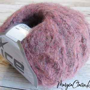 May include: A ball of dusty rose-colored yarn with flecks of darker hues. The yarn has a soft, fuzzy texture. A label with the brand name "ice" is partially visible. The words "Maryia Claire Knits" are written in cursive on the bottom right.