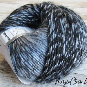 May include: A ball of Rihanna brand yarn in shades of black, gray, and light blue. The yarn has a textured appearance and is partially wrapped with a label. The label includes the brand name and other details. The yarn is on a light wood surface.