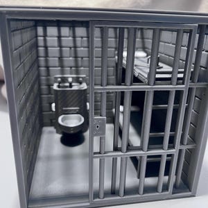 Pode incluir: Um diorama em miniatura de cela de prisão impresso em 3D na cor cinza, apresentando uma porta de grades deslizante com fechadura, paredes com textura de tijolo, um pequeno vaso sanitário e uma estrutura de beliche. A estrutura é monocromática.