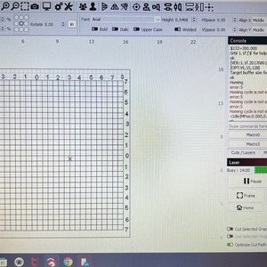 Pode incluir: Um ecrã de computador que exibe uma interface de software de corte a laser. A interface inclui uma grelha, painéis de controlo e texto. O ecrã mostra configurações, comandos e uma barra de progresso. O software é usado para projetos de gravação e corte a laser.