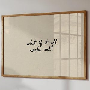 Peut inclure: Impression encadrée avec un fond beige clair et le texte manuscrit "what if it all works out?" en cursive noire. Le cadre est en bois brun clair. L'impression est affichée sur un mur blanc.