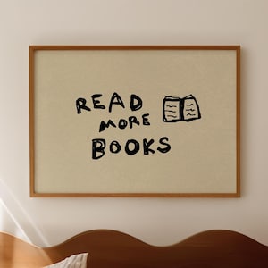 May include: A framed print with the words "READ MORE BOOKS" in black, with a small book illustration. The print hangs above a bed with striped bedding and a wooden headboard. The room has a neutral color palette.