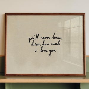 Puede incluir: Una impresión enmarcada con el texto escrito a mano "you'll never know, Dear, how much I love you." El marco es marrón y la impresión se muestra en un estante verde y beige fijado a una pared blanca.
