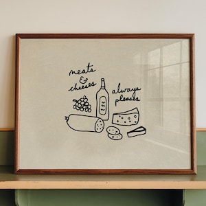 May include: A framed print with a brown wooden frame featuring a black and white illustration of meats, cheeses, and a bottle of wine. The text "meats & cheeses always pleases" is written on the print. The frame rests on a green and beige shelf.