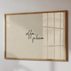 May include: A framed print with the words "coffee, please" in elegant cursive script. The print has a neutral background and is encased in a light brown wooden frame. The artwork is mounted on a white wall.