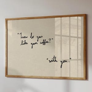 Puede incluir: Impresión enmarcada con la pregunta "How do you like your coffee?" y la respuesta "with you." El texto manuscrito negro está sobre un fondo beige, en un marco de madera marrón claro.