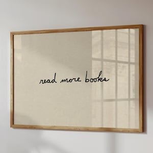 Pode incluir: Impressão emoldurada com as palavras "read more books" em escrita preta sobre um fundo bege. A moldura é de madeira castanha clara. A impressão está pendurada numa parede branca.