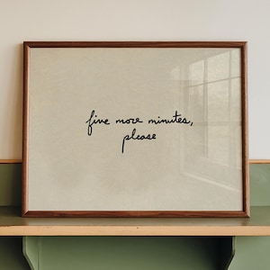 Può includere: Una stampa incorniciata con il testo "five more minutes, please" in stile scritto a mano. La cornice è marrone e la stampa è esposta su una mensola verde e beige fissata a una parete bianca. La mensola ha un design arrotondato.