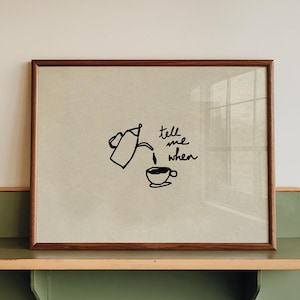 Peut inclure: Une impression encadrée avec un cadre en bois marron, représentant une illustration noire d'une théière versant dans une tasse à thé, avec les mots "tell me when" en écriture noire. L'impression est affichée sur une étagère verte et bois.