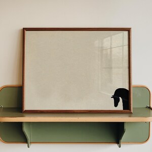 May include: A framed artwork with a brown wooden frame, featuring a black silhouette of a swan. The artwork rests on a green and tan shelf with a curved design, mounted on a white wall. The shelf has a lower shelf.