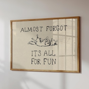 Puede incluir: Una impresión enmarcada con el texto "ALMOST FORGOT IT'S ALL FOR FUN" en negro. Una ilustración de un perro está encima del texto. La impresión tiene un fondo beige claro y un marco de madera.