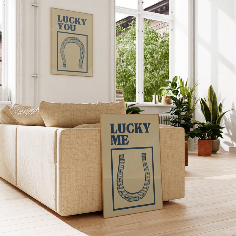 Puede incluir: Dos impresiones enmarcadas con fondo beige y texto azul. La impresi&oacute;n superior dice "Lucky You" y la impresi&oacute;n inferior dice "Lucky Me". Ambas impresiones presentan un gr&aacute;fico de herradura azul.