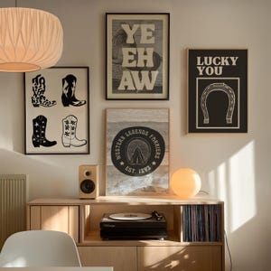 May include: A selection of framed art prints with a Western theme. The prints feature cowboy boots, the text "YE HAW", a horseshoe with the text "LUCKY YOU", and a circular emblem with the text "WESTERN LEGENDS FARRIERS EST. 1893".