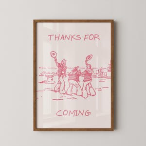 May include: A framed wall art print featuring a light pink background with a dark pink line drawing of three figures in sailor-style clothing waving hats. The text "THANKS FOR" appears above the figures and "COMING" is printed below them.
