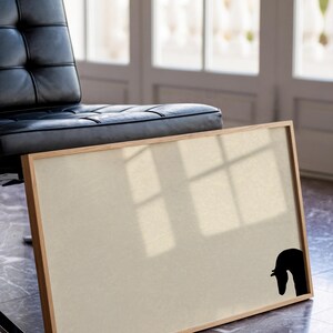 May include: A rectangular framed artwork with a beige canvas and a black horse head silhouette in the lower right corner. The frame is made of light-colored wood. A black leather chair is in the background.