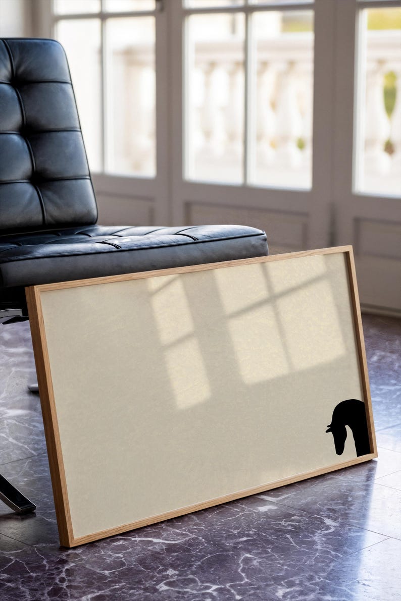 May include: A rectangular framed artwork with a beige canvas and a black horse head silhouette in the lower right corner. The frame is made of light-colored wood. A black leather chair is in the background.