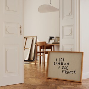 Puede incluir: Una obra de arte enmarcada con el texto "I SEE LONDON I SEE FRANCE" en fuente manuscrita negra. La obra de arte est&aacute; en una habitaci&oacute;n con suelo de madera, una silla de madera y un escritorio con libros. La habitaci&oacute;n tiene paredes blancas y una gran puerta blanca.