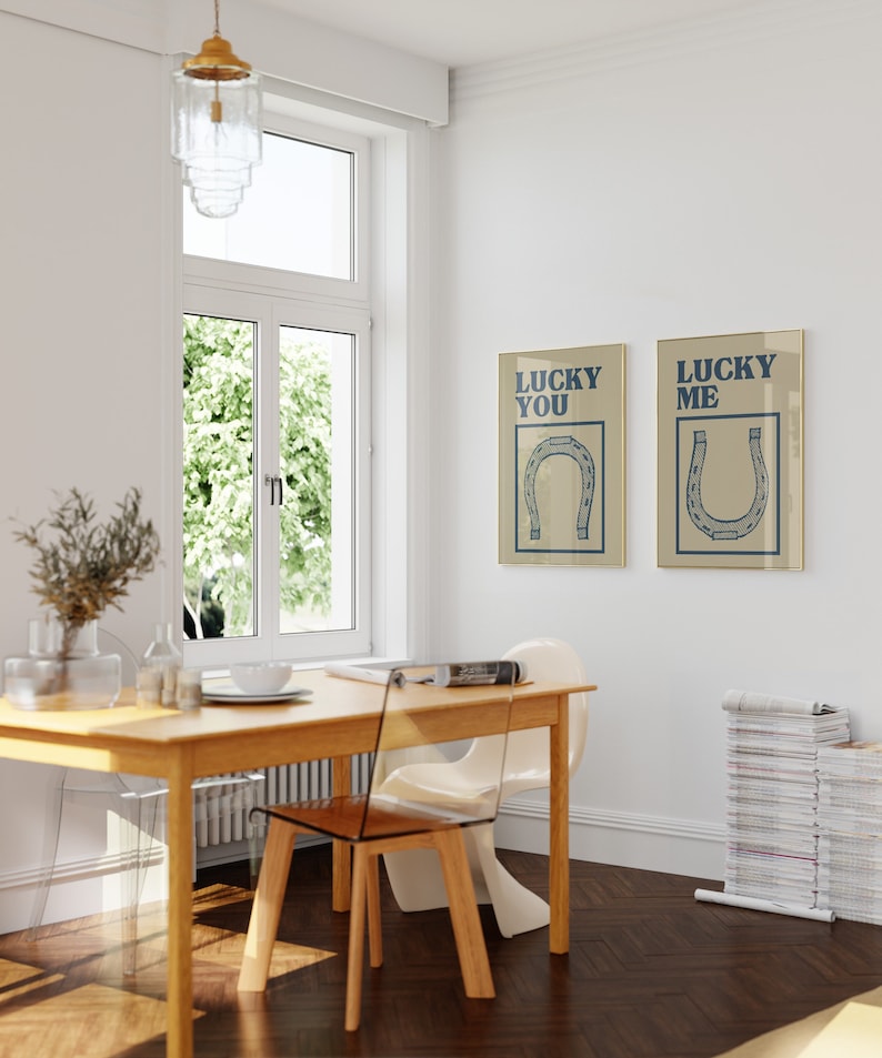 Puede incluir: Dos impresiones enmarcadas en beige con texto azul e ilustraciones de herraduras. El texto de la impresi&oacute;n de la izquierda dice "Lucky You" y el texto de la impresi&oacute;n de la derecha dice "Lucky Me".