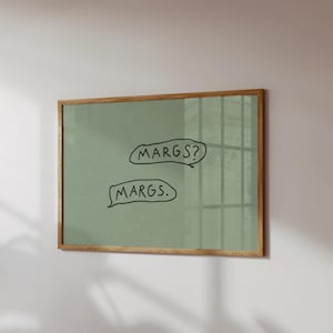 May include: A framed artwork with a light green background and a natural wood frame. The artwork features two speech bubbles with the handwritten text "MARGS?" and "MARGS." The piece is mounted on a white wall.