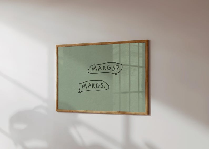 May include: A framed artwork with a light green background and a natural wood frame. The artwork features two speech bubbles with the handwritten text "MARGS?" and "MARGS." The piece is mounted on a white wall.