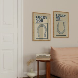 Puede incluir: Dos impresiones enmarcadas con fondo beige y texto azul. El texto de la impresi&oacute;n de la izquierda dice "Lucky You" y el texto de la impresi&oacute;n de la derecha dice "Lucky Me". Ambas impresiones presentan una ilustraci&oacute;n de herradura azul.