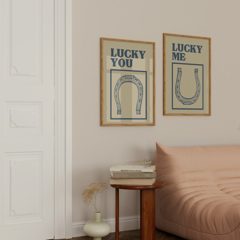Puede incluir: Dos impresiones enmarcadas con fondo beige y texto azul. El texto de la impresi&oacute;n de la izquierda dice "Lucky You" y el texto de la impresi&oacute;n de la derecha dice "Lucky Me". Ambas impresiones presentan una ilustraci&oacute;n de herradura azul.