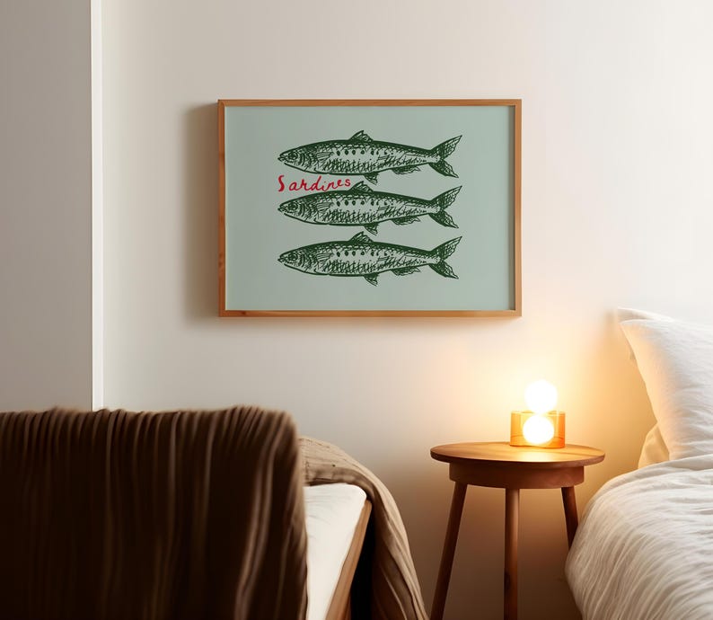 May include: A framed art print featuring three green fish illustrations on a light blue background. The word "Sardines" is written in red script above the fish. The frame is made of wood.