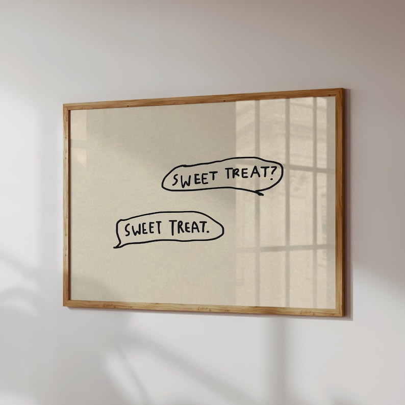 May include: A framed print with a light beige background. Two speech bubbles contain the handwritten text "SWEET TREAT?" and "SWEET TREAT." The frame is made of light brown wood.