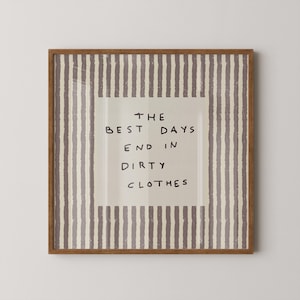Peut inclure: Un cadre en bois marron contenant une impression. Le fond crème porte l'inscription noire « THE BEST DAYS END IN DIRTY CLOTHES ». Le fond est orné de rayures verticales grises et blanches.