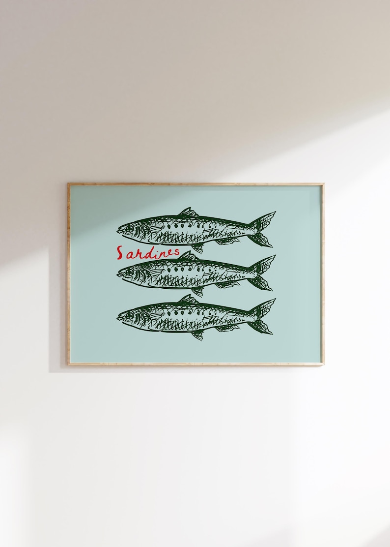 May include: A framed art print featuring three stylized green sardines on a light blue background. The word "Sardines" is written in red script. The artwork has a minimalist, illustrative style, suitable for kitchen or dining decor.