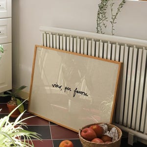 May include: A framed artwork with the text "vino, per favore" sits against a white radiator. A woven basket filled with red apples and a single apple are on a black and red tiled floor. A potted plant is in the foreground.