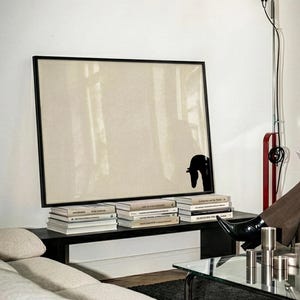 May include: A modern living room scene featuring a large framed artwork with a black silhouette, stacked books, and a black table. A floor lamp with a red accent and a glass-topped coffee table are also visible.