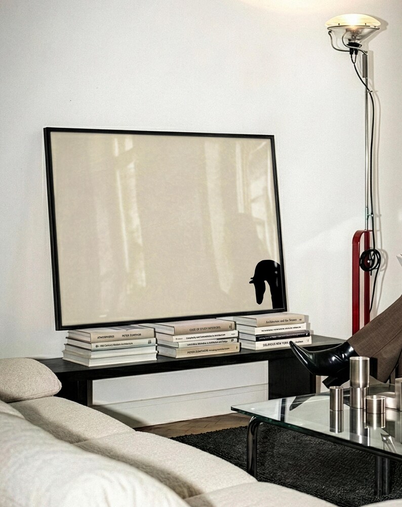 May include: A modern living room scene featuring a large framed artwork with a black silhouette, stacked books, and a black table. A floor lamp with a red accent and a glass-topped coffee table are also visible.