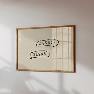 May include: A framed print with a beige background and a light brown wooden frame. The print features two speech bubbles with the words "JESUS?" and "JESUS." written in black, handwritten-style font. The artwork is mounted on a white wall.