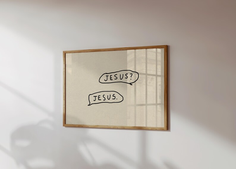 May include: A framed print with a beige background and a light brown wooden frame. The print features two speech bubbles with the words "JESUS?" and "JESUS." written in black, handwritten-style font. The artwork is mounted on a white wall.