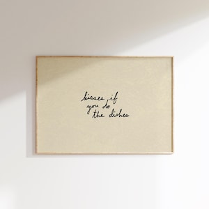 May include: A framed print with a light beige background and the handwritten text "kisses if you do the dishes" in black cursive. The frame is a light brown color.
