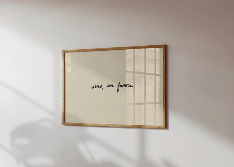 May include: A framed print with the words "vino, per favore" in black script on a beige background. The frame is made of light brown wood. The print is hanging on a white wall.