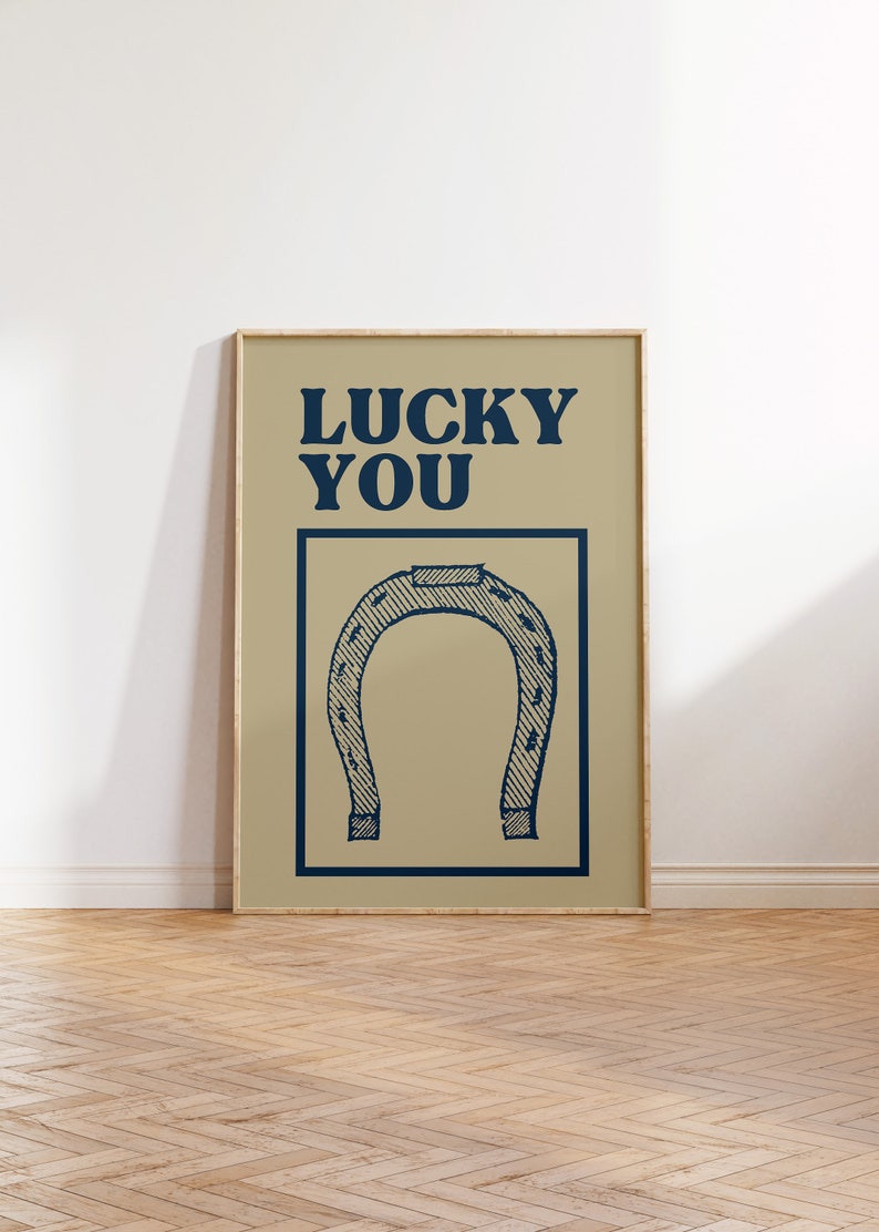 Puede incluir: Un p&oacute;ster beige con marco de madera presenta una herradura azul y el texto "LUCKY YOU" en letras azules en negrita.