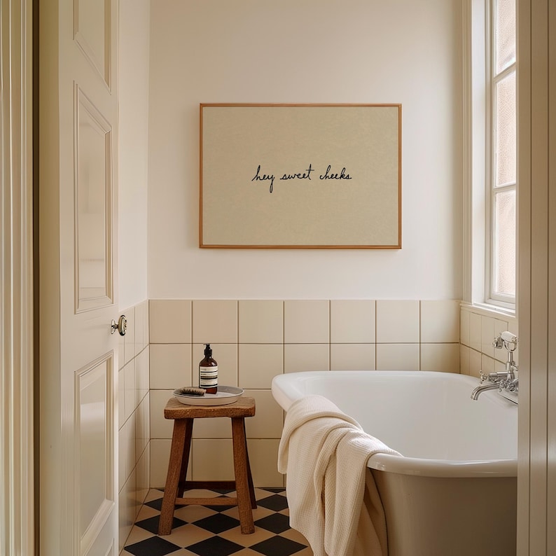 May include: A bathroom scene featuring a framed print with the text "hey sweet cheeks". The room includes a white bathtub, a wooden stool with a bottle and brush, and a black and white checkered floor. A cream-colored towel hangs on the tub.