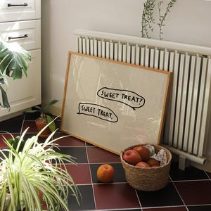 May include: A framed artwork with the text "SWEET TREAT?" and "SWEET TREAT." is propped against a white radiator. A woven basket filled with red apples sits nearby. A single apple rests on the floor. The scene is set on a red and black tiled floor.