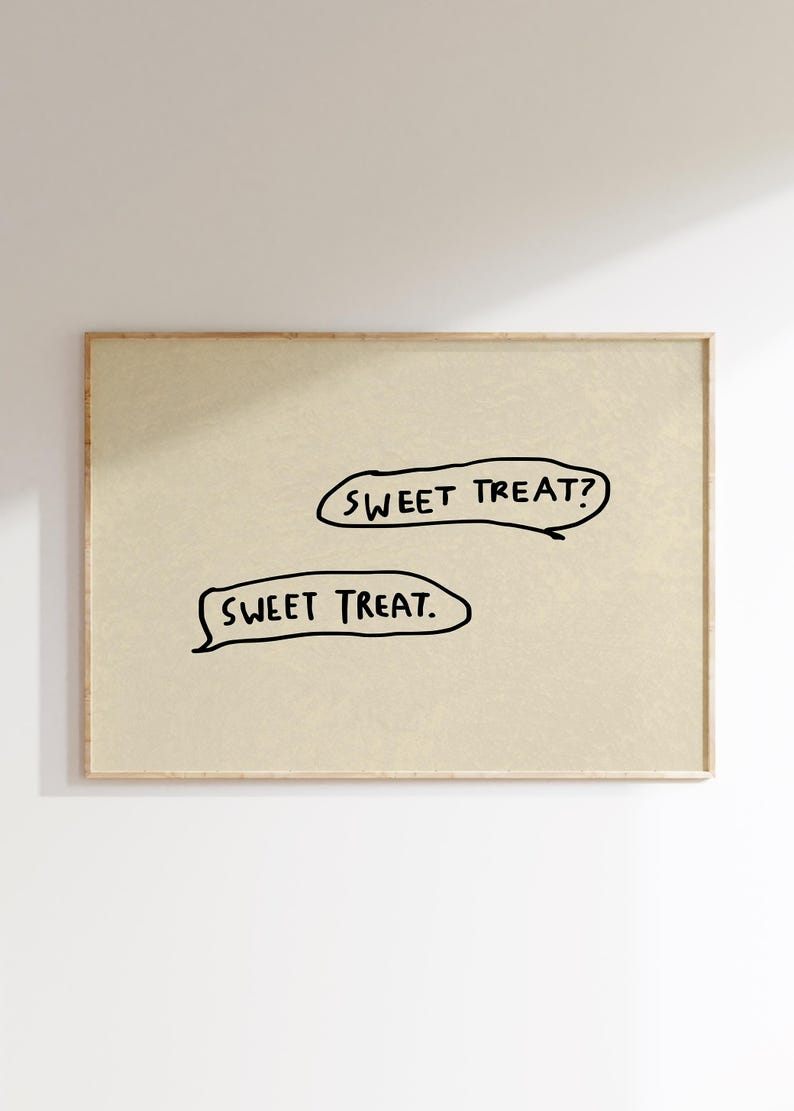 May include: A framed print featuring the text "SWEET TREAT?" and "SWEET TREAT." in black, handwritten-style lettering. The background is a light beige color, and the frame is a natural wood tone. The artwork is simple and modern.