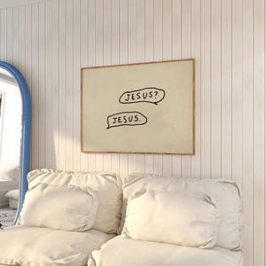May include: A framed print with the text "JESUS?" and "JESUS." in black speech bubbles. The artwork has a beige background and a brown frame. The print hangs on a white paneled wall above a white sofa with pillows.