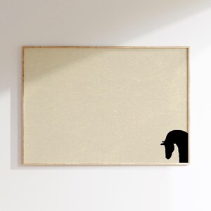 May include: A framed art print featuring a minimalist design. The artwork showcases a black silhouette of a horse's head in the lower right corner against a beige background. The frame is made of light-colored wood.
