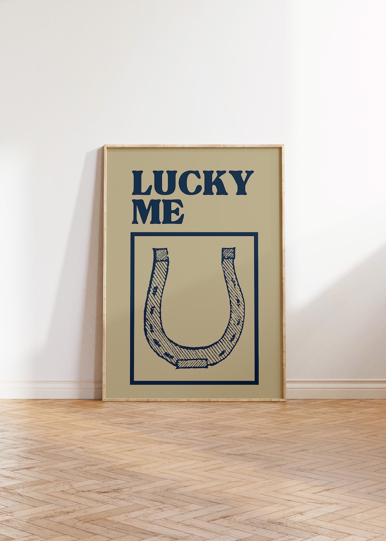 Puede incluir: Un p&oacute;ster beige con marco de madera que presenta una herradura azul y el texto "LUCKY ME" en azul.