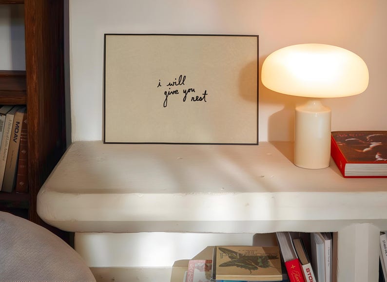 Puede incluir: Una taza de cer&aacute;mica blanca con asa negra y el texto "But First, Coffee" en negrita negra. La taza se encuentra sobre un fondo borroso, sugiriendo un ambiente acogedor.