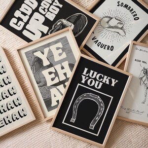May include: A selection of framed art prints with a Western theme. The prints feature bold text and illustrations, including a cowboy hat, horseshoe, and horse. The colour palette is primarily black, white, and beige, with wooden frames.