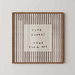 May include: A square wall art piece in a wooden frame featuring a beige centre panel with the black handwritten text CUTE SHOES! TAKE THEM OFF. The border consists of vertical, textured, dark mauve and cream stripes surrounding the central text.