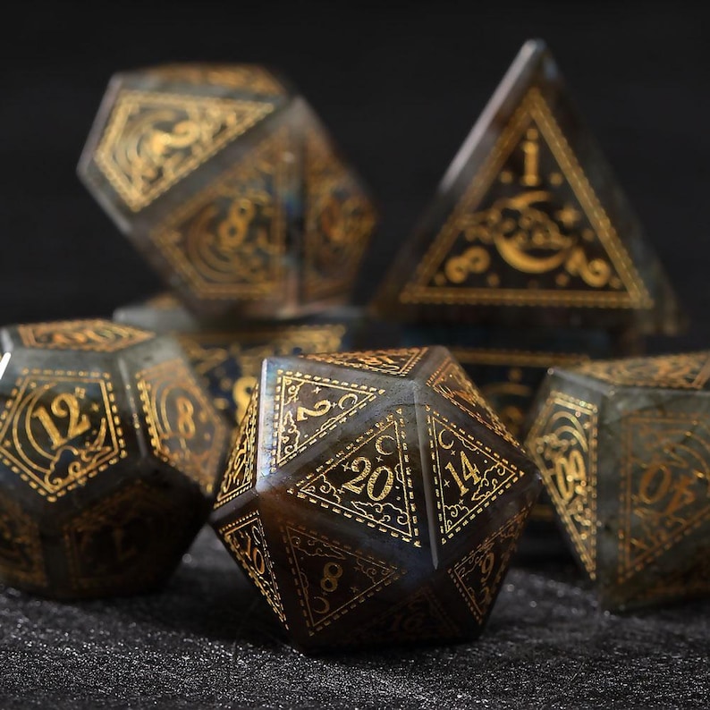 May include: Set of gemstone dice with gold-colored numbering and decorative designs. The dice are various polyhedral shapes, including a d20, d12, and d4. The dice have a dark, iridescent base color.