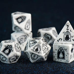 Pode incluir: Um conjunto de dados poliédricos com padrão de mármore branco, apresentando ilustrações em tinta preta de fantasmas dentro de arcos góticos e pequenos morcegos. O conjunto inclui formas como d20, d12, d10, d8, d6 e d4 com números pretos.
